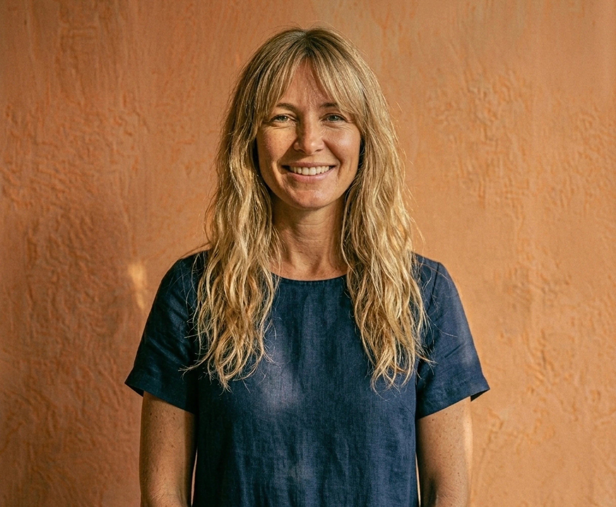 Woman with blond hair, smiling in front of a beige wall